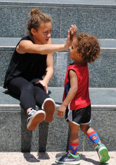 Two children high-fiving each other atop granite stairs