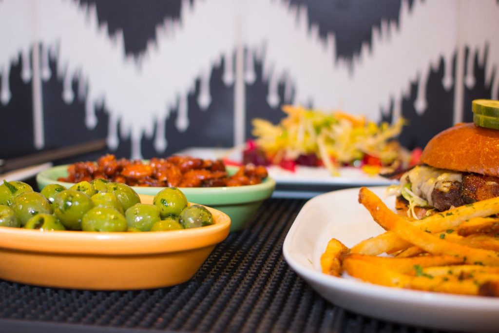 Plate of delicious french fries and burger beside plate of marinated olives served at Perch + Plow