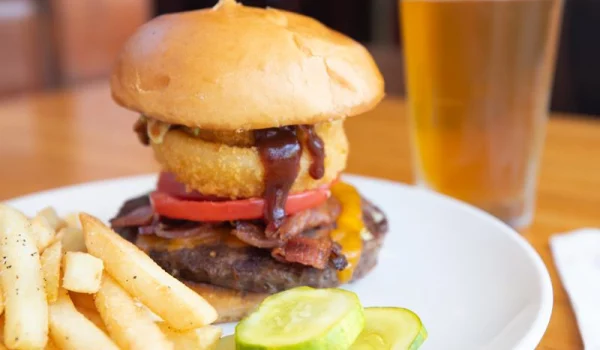 Plate of delicious french fries and burger topped with onion rings next to a small stack of pickles served at McNear's Saloon and Dining Hall