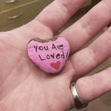 Person holding small heart shaped painted rock with 