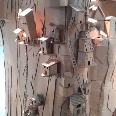 Cardboard sculpture of small houses built into cliffside
