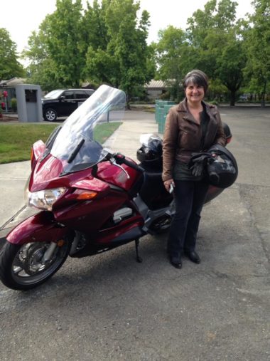 woman in brown leathers holding helmet by motorcycle