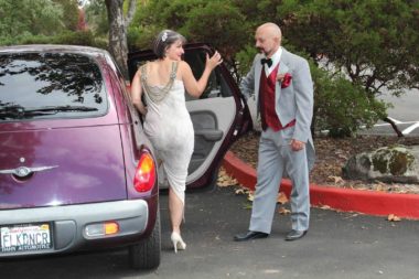 woman in fancy scoop-back dress stepping into car as tuxedoed man stands at door