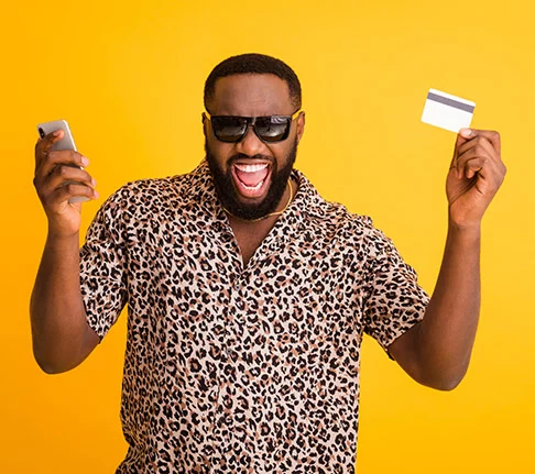 grinning African-American man in sunglasses holding credit card in one hand, phone in other