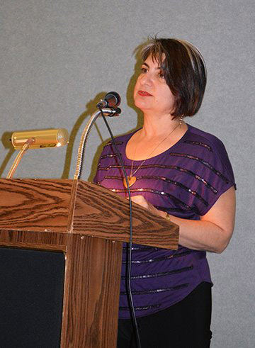 woman in purple top behind podium at mic